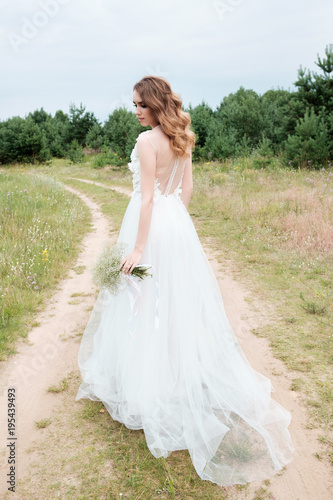 bride in white llight wedding dress with bridal bouquet walking in lane, back view