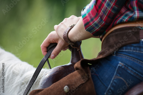 The cowboy on a white horse in western style holds the reins. Detail closeup