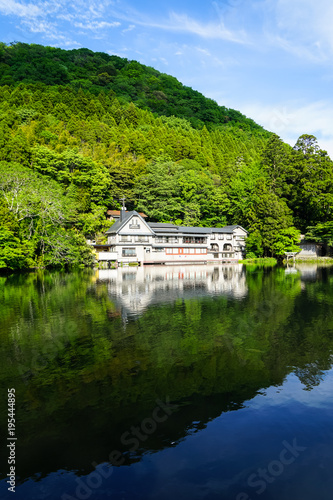 Beautiful abundant natural shades of spring green mountain background mirror reflection on fresh lake Kinrinko with buildings and blue sky, Yufuin
