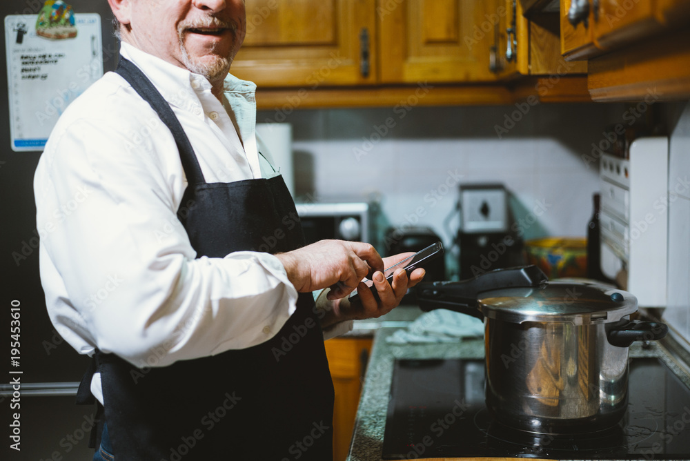 Man of 59 year old with smartphone in the kitchen of his house. Man of 59 year old with smartphone in the kitchen of his house.