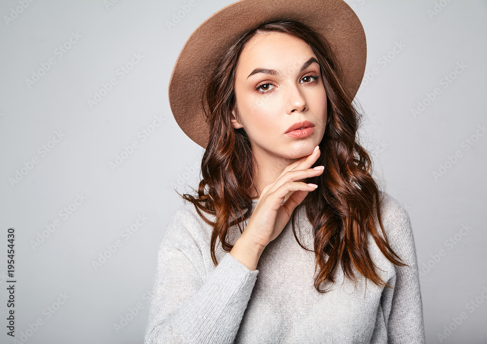 Horizontal portrait of stylish attractive female model wears summer clothes and brown hat with natural makeup posing on gray background in studio. Looking at camera Horizontal portrait of stylish attractive female model wears summer clothes and brown hat with natural makeup posing on gray background in studio. Looking at camera