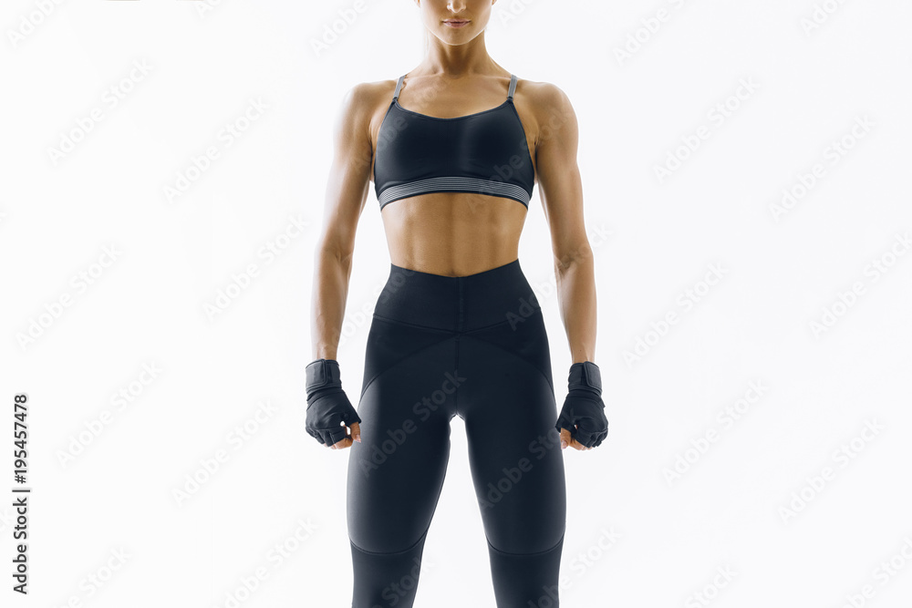 Cropped concept portrait of strong woman in black athletic garments stands against a white background and looks confident at camera Cropped concept portrait of strong woman in black athletic garments stands against a white background and looks confident at camera