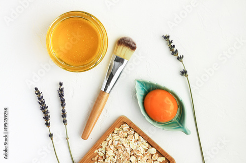 Nourishing skin care natural treatment, facial mask with egg yolk, honey, oat flakes, ingredients viewed from above on simple white background.