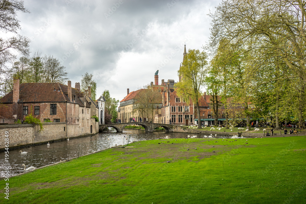 Bruges (Brugge) canal with swan at bridge and gate to Beguinage (Prinselijke Begijnhof van Wijngaerde)