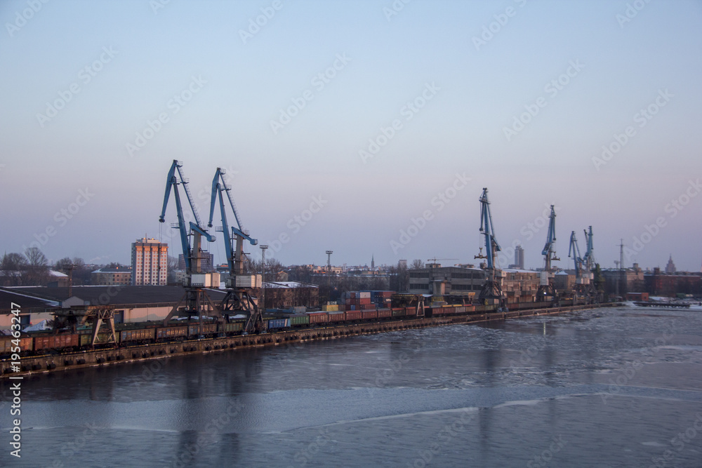 Freight shipping containers and gas oil tanks at the docks. in import export and business logistic. Cargo ship docked at at the port. Cargo cranes by winter evening in the Port Riga, Latvia. Freight shipping containers and gas oil tanks at the docks. in import export and business logistic. Cargo ship docked at at the port. Cargo cranes by winter evening in the Port Riga, Latvia.