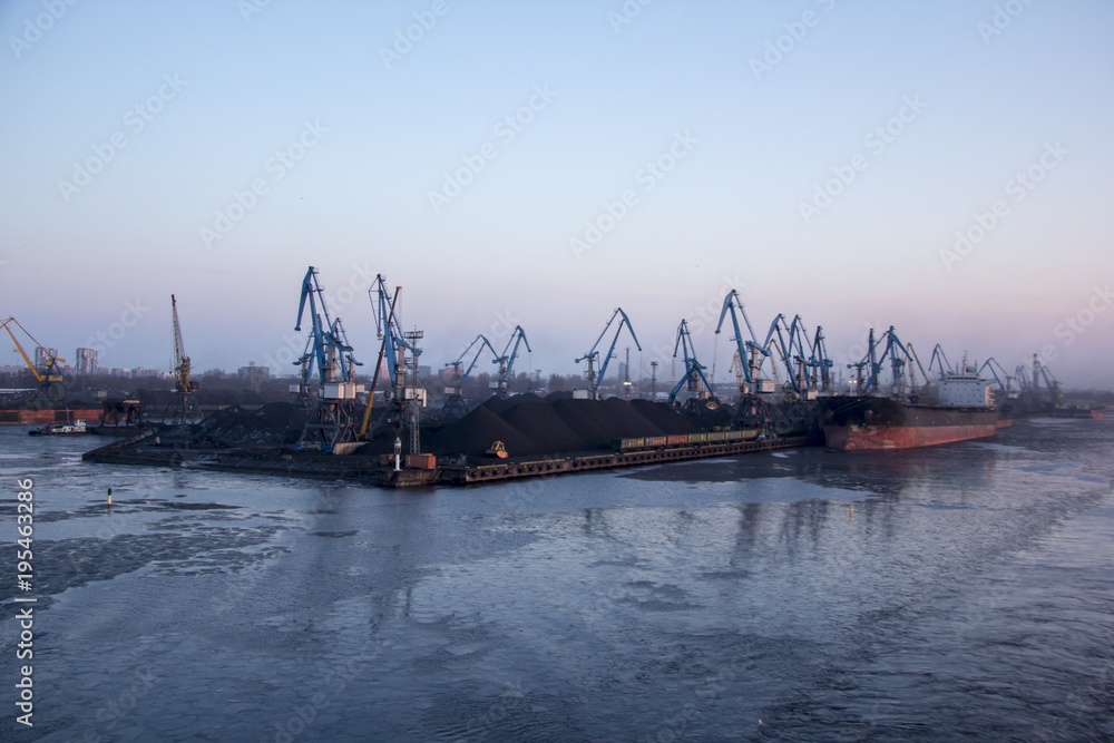 Fototapeta premium Freight shipping containers and gas oil tanks at the docks. in import export and business logistic. Cargo ship docked at at the port. Cargo cranes by winter evening in the Port Riga, Latvia.