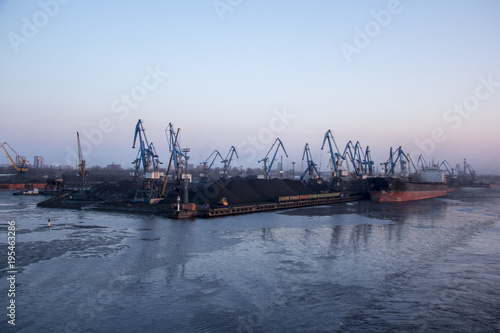 Freight shipping containers and gas oil tanks at the docks. in import export and business logistic. Cargo ship docked at at the port. Cargo cranes by winter evening in the Port Riga, Latvia. © Uldis