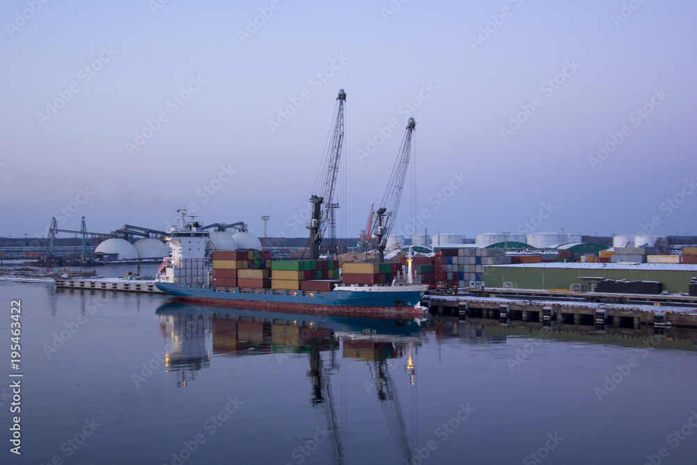 Freight shipping containers and gas oil tanks at the docks. in import export and business logistic. Cargo ship docked at at the port. Cargo cranes by winter evening in the Port Riga, Latvia.