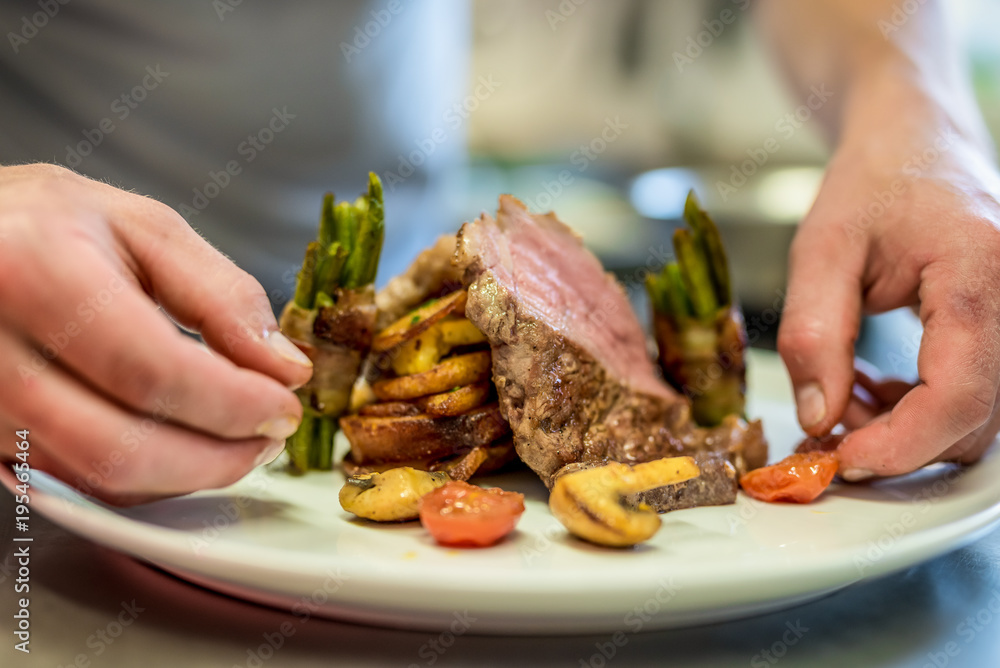 Closeup of the hands of a chef decorating a meat steak
