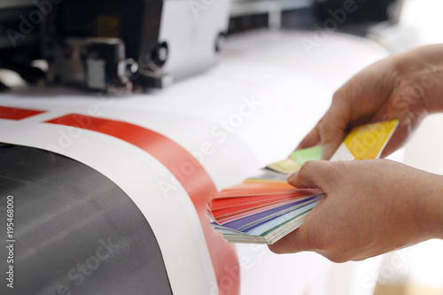 Maszyna drukarska, kolorowy wydruk. Drukarz sprawdza kolor wydruku na próbniku kolorów.