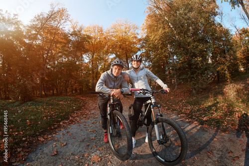Happy young couple going for a bike ride on an autumn day in the park, backlight.