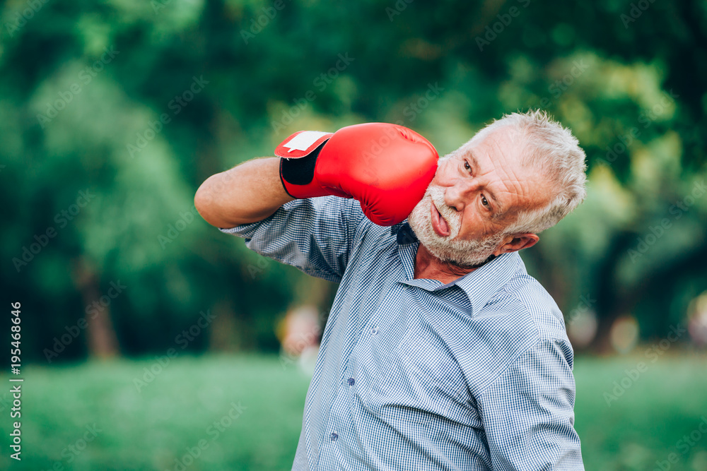 Senior man punching his face with red boxing gloves in nature background