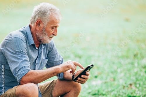 Senior men using a smartphone while sitting on grass in the park