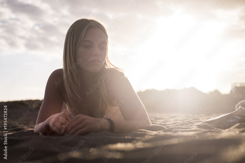 blonde young woman lay down on the beach with sun backlight