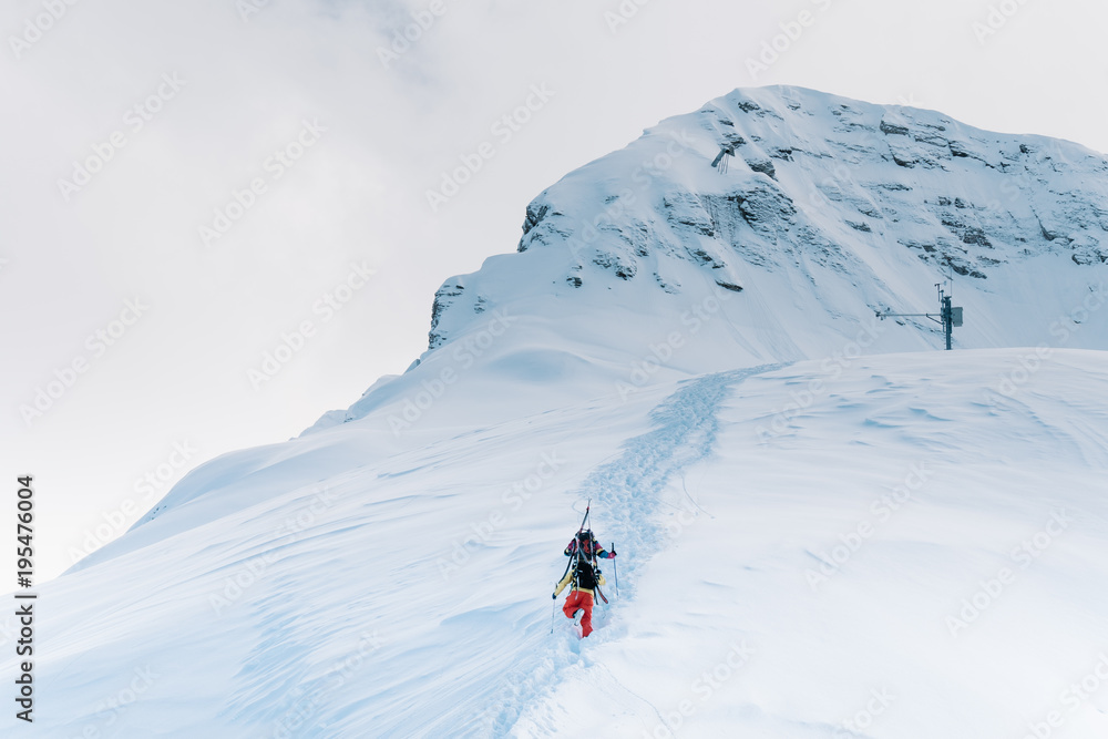 Two skiers in color suits climb a high mountain