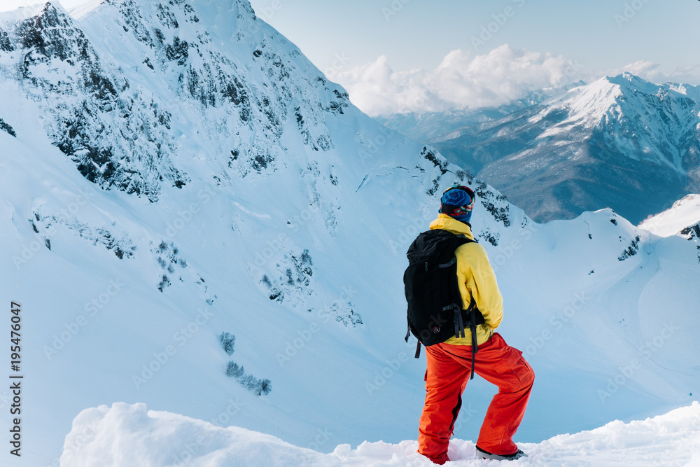 Skier in a colored suit with a backpack looking at the mountains