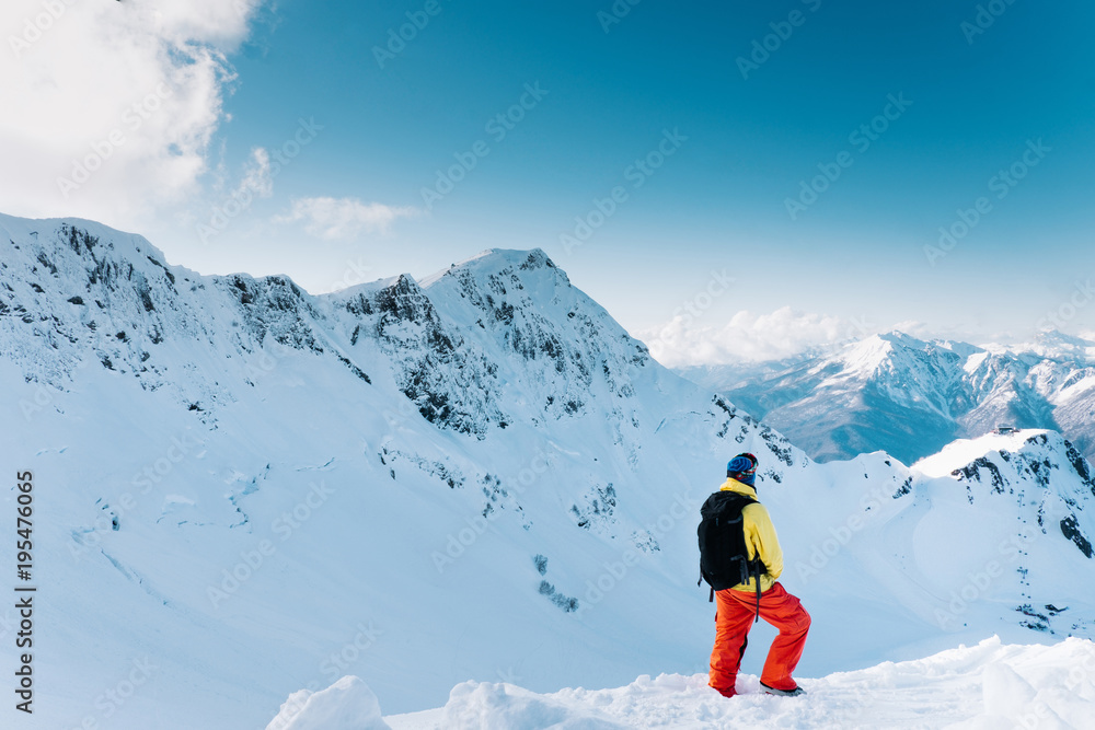 skier in colored suit with a backpack standing on the background of beautiful mountains