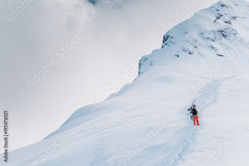 Two skiers in multi-colored suits climb a high snow mountain