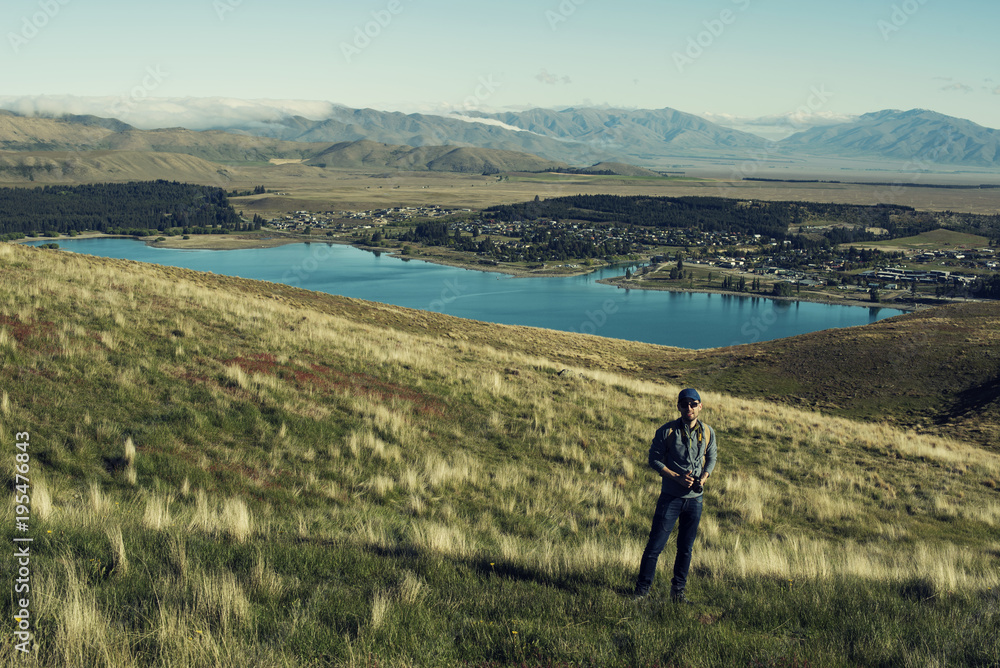 Retrato de hombre joven frente a vista de ciudad a la orilla de un gran lago en una zona montañosa con nubes aproximándose.