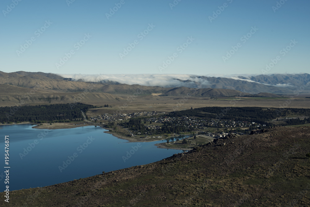 Vista de ciudad a la orilla de un gran lago en una zona montañosa con nubes aproximándose.