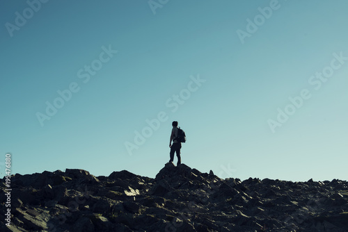Retrato de hombre a contraluz en la cima de una monta  a rocosa. Cielo azul al atardecer.