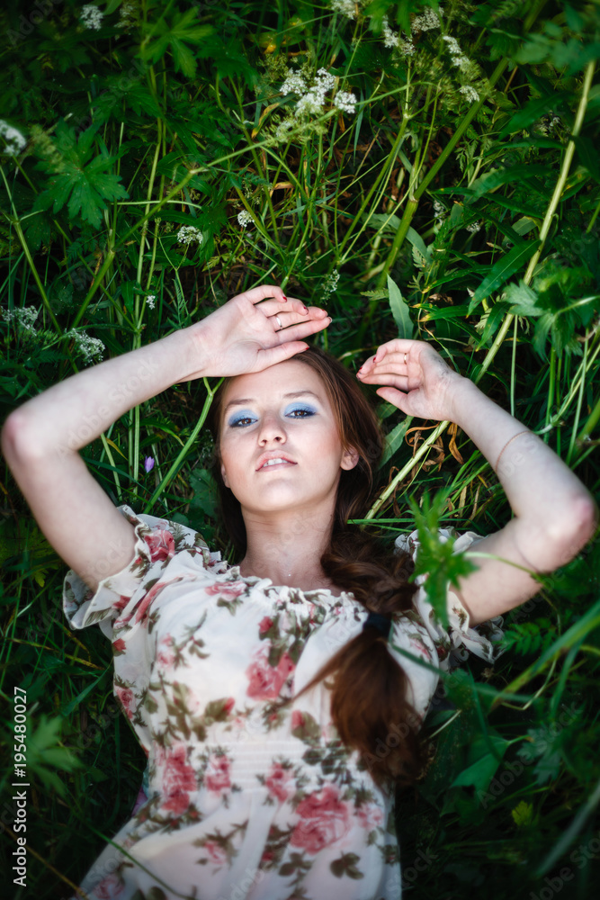 A beautiful girl in a light dress lies in a tall grass and looks into the sky. Young woman lying on the grass to relax a little. Top view, with space for text. A beautiful girl in a light dress lies in a tall grass and looks into the sky. Young woman lying on the grass to relax a little. Top view, with space for text.