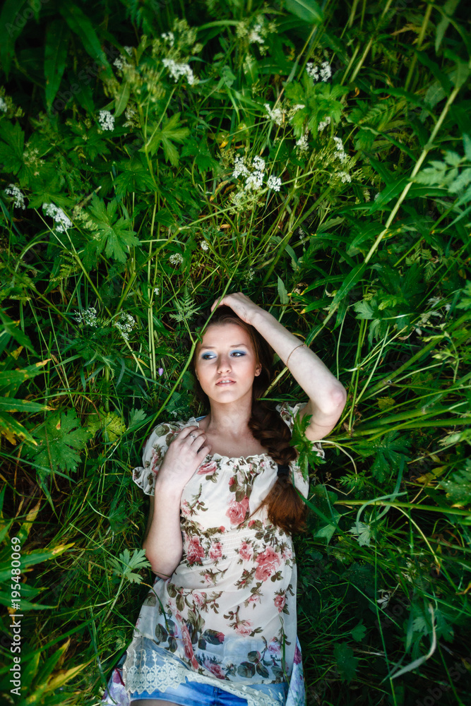 A beautiful girl in a light dress lies in a tall grass and looks into the sky. Young woman lying on the grass to relax a little. Top view, with space for text. A beautiful girl in a light dress lies in a tall grass and looks into the sky. Young woman lying on the grass to relax a little. Top view, with space for text.
