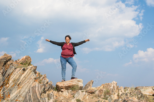 Asian woman standing on colorful rocks with her arms up in the a