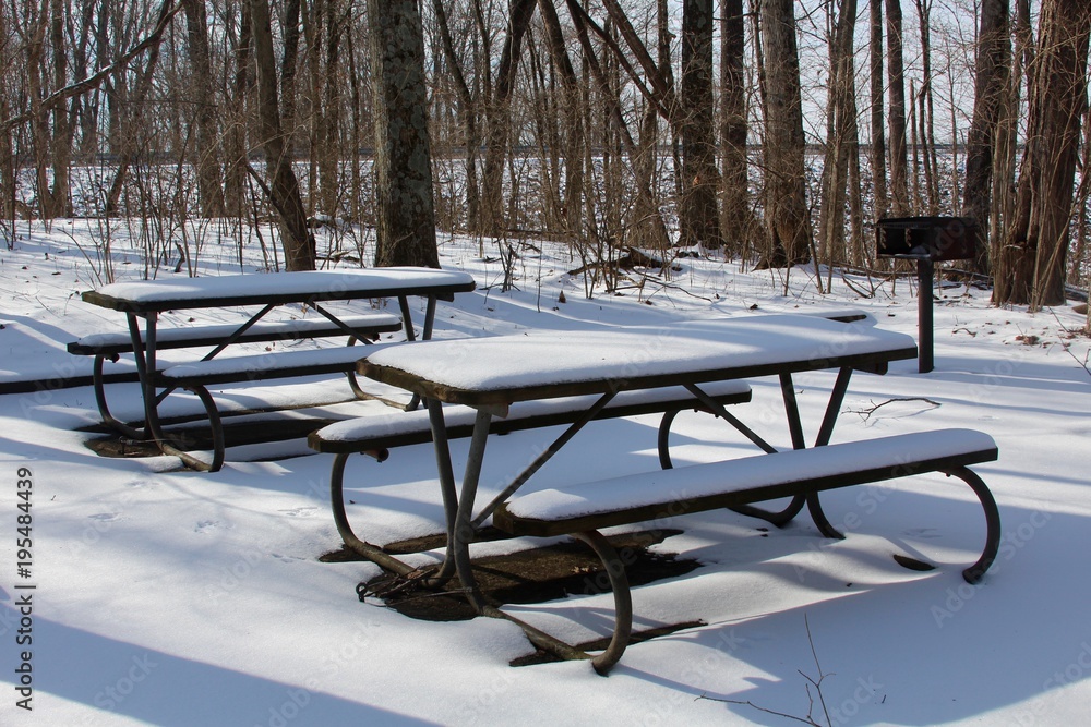 The snow covered picnic tables on a close view.