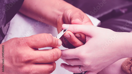 Manicurist using pliers to remove dead skin from around the client fingers. 