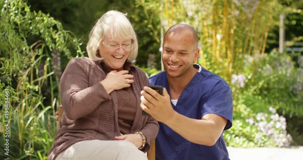 4K Happy mature lady laughing with her caregiver, looking at photos on a smartphone. Slow motion 4K Happy mature lady laughing with her caregiver, looking at photos on a smartphone. Slow motion