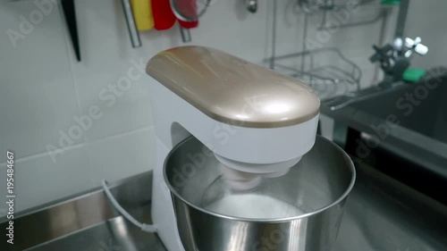 Mixer whipped white cream on table in house kitchen indoors. Eelectric appliance mixes sweet mass in metal bowl on cuisine desk. Compact device works quickly, on ceramic wall in room household objects photo