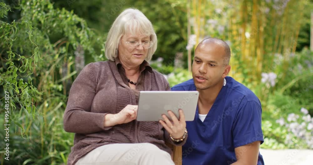 4K Mixed race male nurse teaching senior lady to use digital tablet in the garden of retirement home or medical facility. Slow motion 4K Mixed race male nurse teaching senior lady to use digital tablet in the garden of retirement home or medical facility. Slow motion
