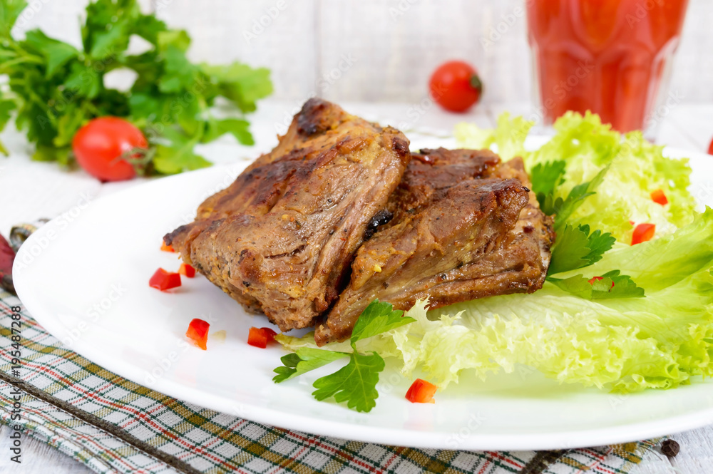Fried pork ribs on a plate with greens and tomato juice on a white wooden background.