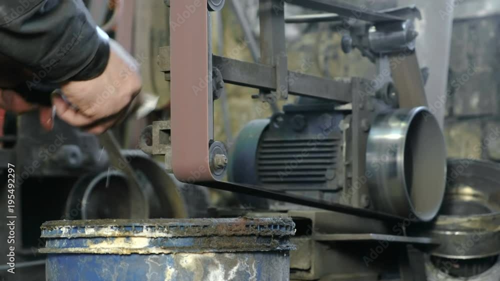 Grinding billets of metal knife on a belt-grinding machine. Close-up of a man's hands. Grinding billets of metal knife on a belt-grinding machine. Close-up of a man's hands.