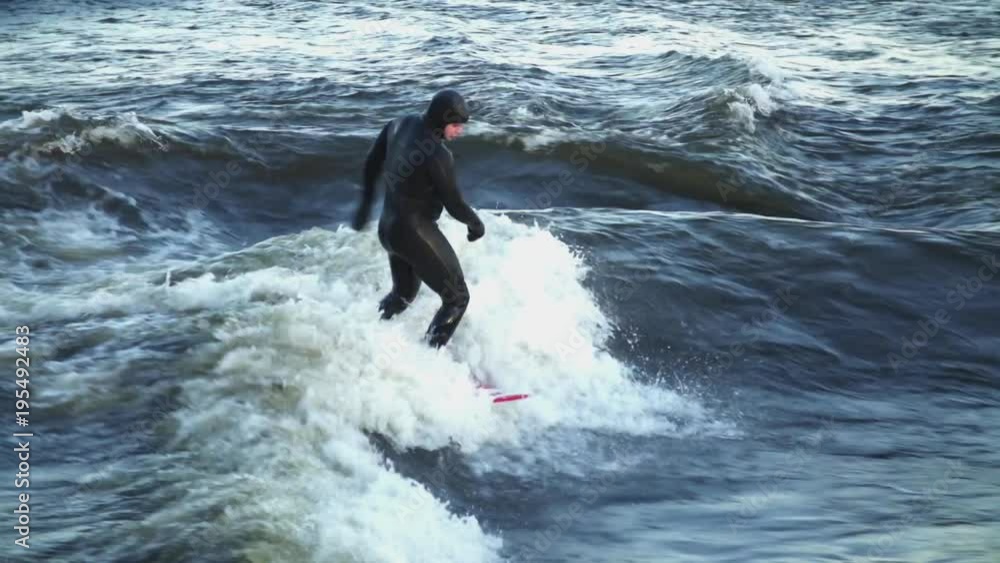 Medium shot of a man surfing in a wave in an icy river then falling Medium shot of a man surfing in a wave in an icy river then falling