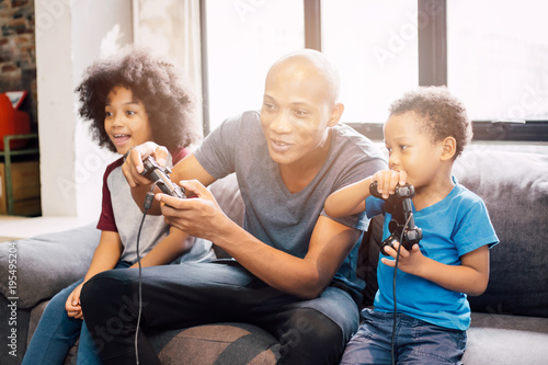 African American family at home sitting in sofa couch and playing console video games together.