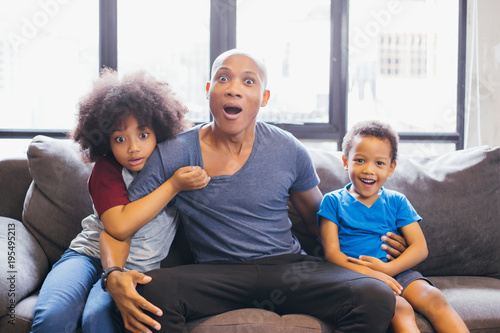 Whole family of African American watching and staring horror movie on TV at home. They are getting frightened and scared. photo