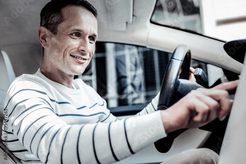 Smart system. Positive joyful good looking man sitting in his car and smiling while pressing a button