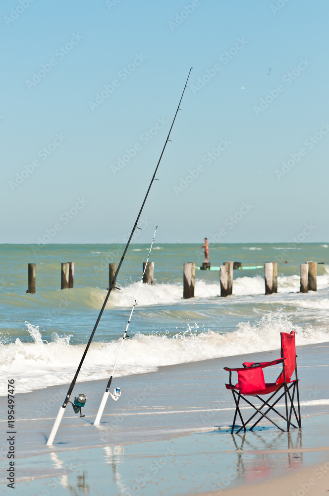 Front view of two surf fishing rods in holders at the shoreline and a red,  beach