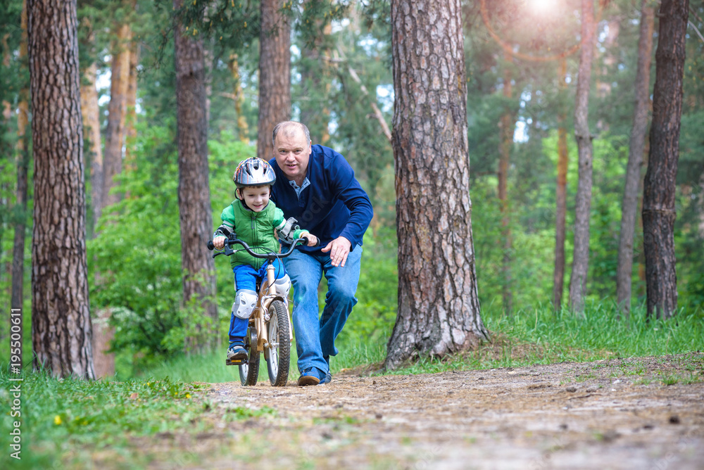 Little kid boy of 3 years and his father in autumn forest with a bicycle. Dad teaching his son. Man happy about success. Child with helmet. Safety, sports, leisure with kids concept. Little kid boy of 3 years and his father in autumn forest with a bicycle. Dad teaching his son. Man happy about success. Child with helmet. Safety, sports, leisure with kids concept.