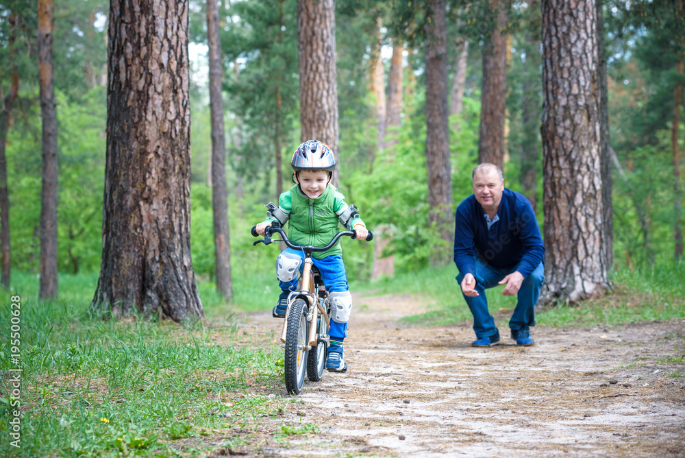Little kid boy of 3 years and his father in autumn forest with a bicycle. Dad teaching his son. Man happy about success. Child with helmet. Safety, sports, leisure with kids concept. Little kid boy of 3 years and his father in autumn forest with a bicycle. Dad teaching his son. Man happy about success. Child with helmet. Safety, sports, leisure with kids concept.