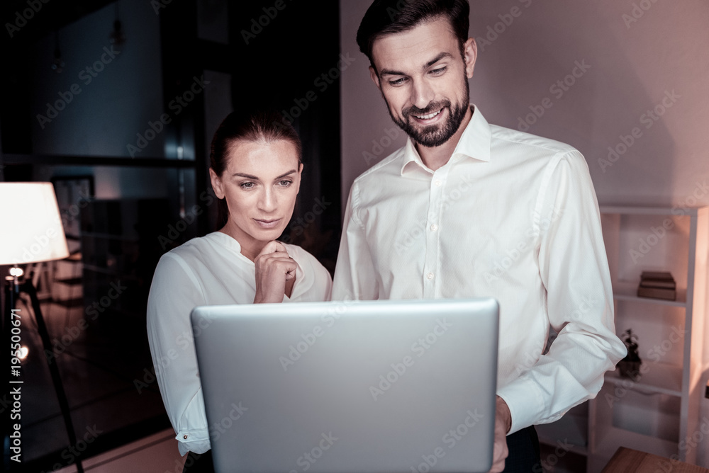Successful project. Pleasant satisfied qualified colleagues standing in the office smiling and looking at the laptop. Successful project. Pleasant satisfied qualified colleagues standing in the office smiling and looking at the laptop.