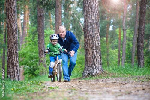 Little kid boy of 3 years and his father in autumn forest with a bicycle. Dad teaching his son. Man happy about success. Child with helmet. Safety, sports, leisure with kids concept.