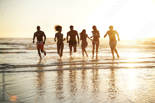 Group Of Friends Run Through Waves Together On Beach Vacation