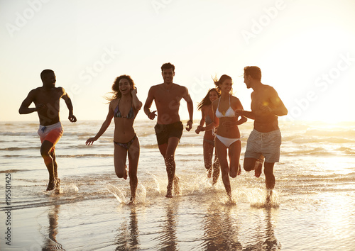 Group Of Friends Run Through Waves Together On Beach Vacation