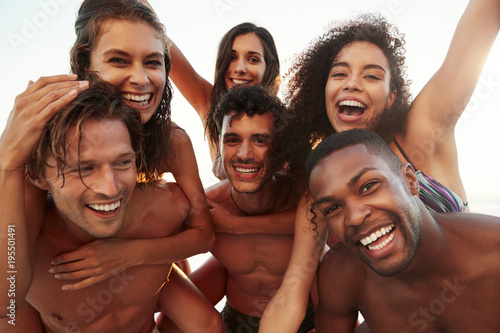 Group Of Friends On Vacation Having Piggyback Race On Beach