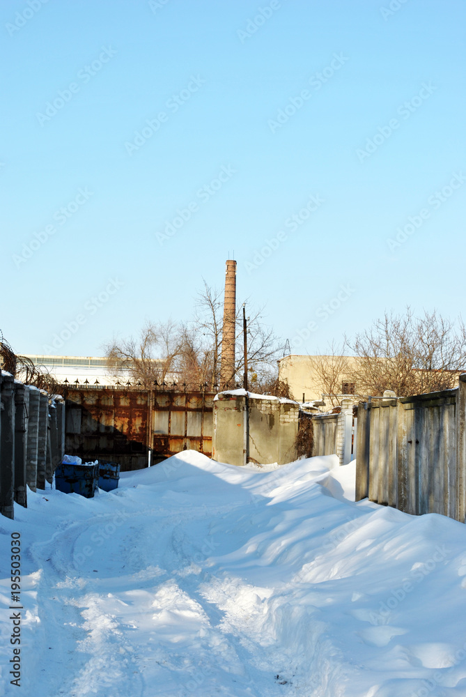 Snowy road along jail barbed wire fence, winter sunny landscape with high pipe in blue sky background