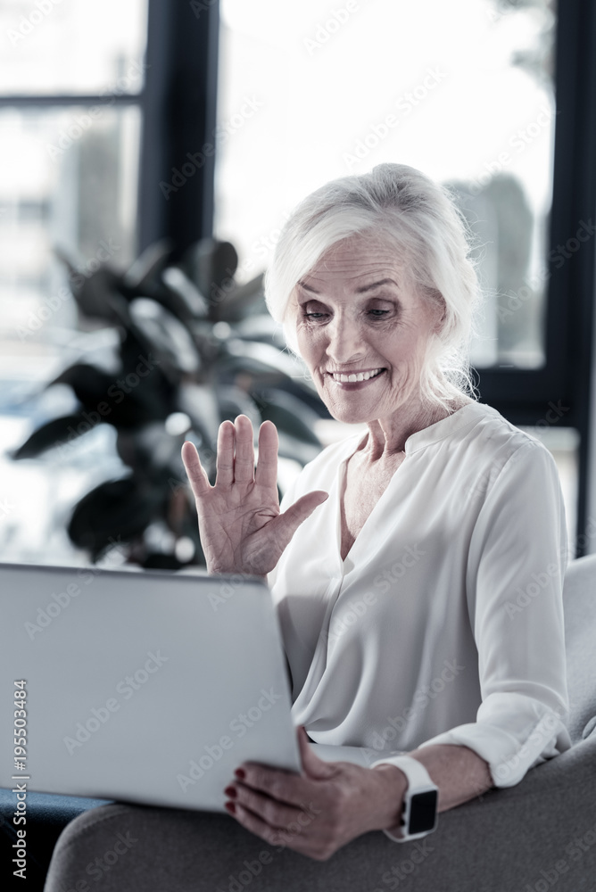 Hello honey. Cheerful senior female person keeping smile on her face and raising eyebrows while looking at computer Hello honey. Cheerful senior female person keeping smile on her face and raising eyebrows while looking at computer