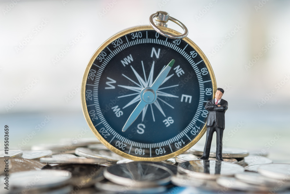 Fototapeta premium Business and planning concept. Businessman miniature figure standing on pile of coins with compass as background.